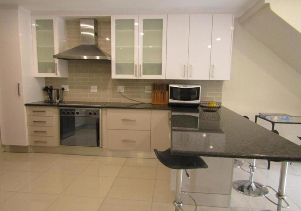 cocina con armarios blancos y encimera negra en Sunninghill Luxury Spacious Executive Penthouse en Sandton