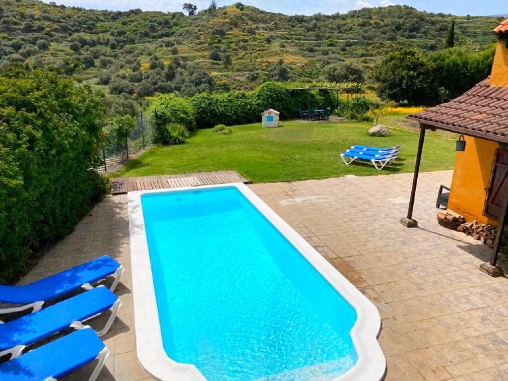 a swimming pool with two blue chairs and a house at Casa Rural CaChispita in Teror