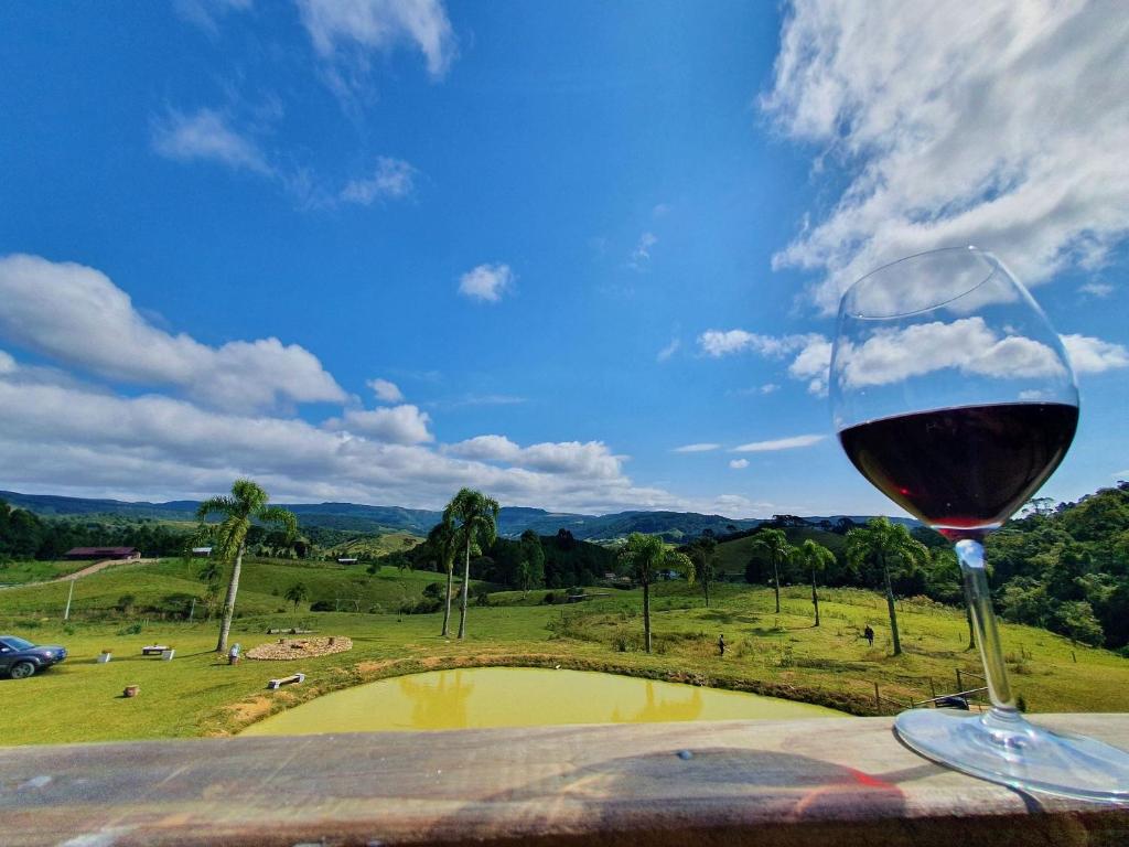 a glass of wine sitting on a table with a view of a field at Cabana Pôr-do-Sol - Rancho Queimado/SC in Rancho Queimado