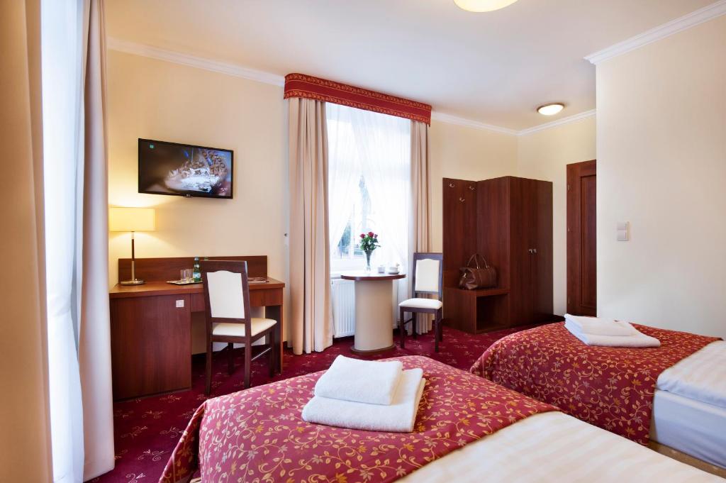 a hotel room with two beds and a desk at Resort de Esperanto Sanatorium Uzdrowiskowe in Duszniki Zdrój