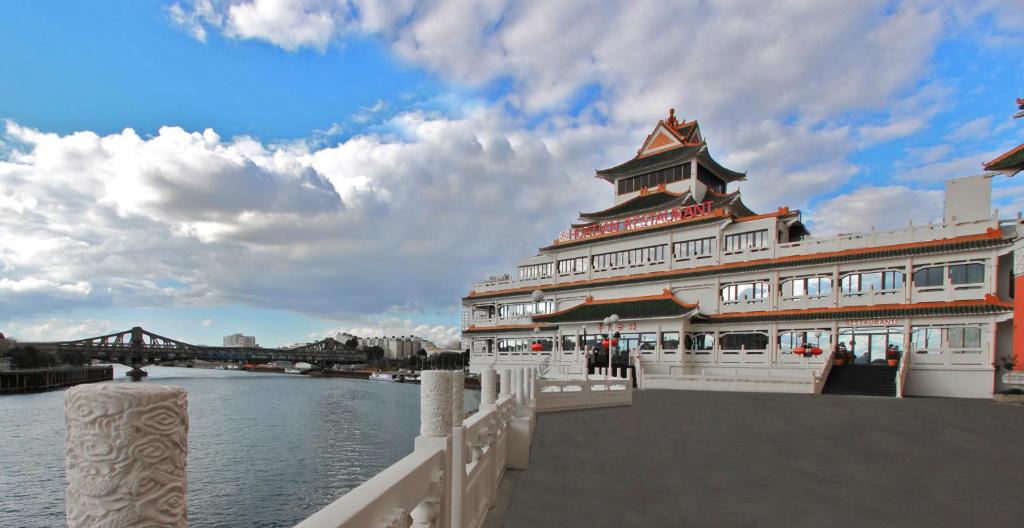 un gran edificio junto a un río con un puente en Hôtel Huatian Chinagora en Alfortville