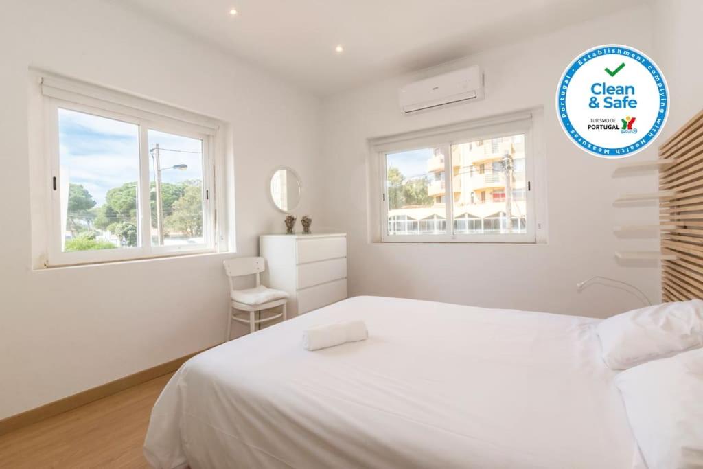 a white bedroom with a white bed and two windows at 4 bedroom apartment near the beach! in Setúbal