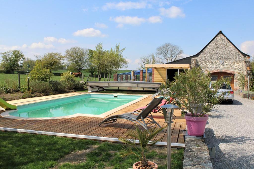 a pool with a wooden deck next to a house at le clos du fourmanoir in Avesnelles