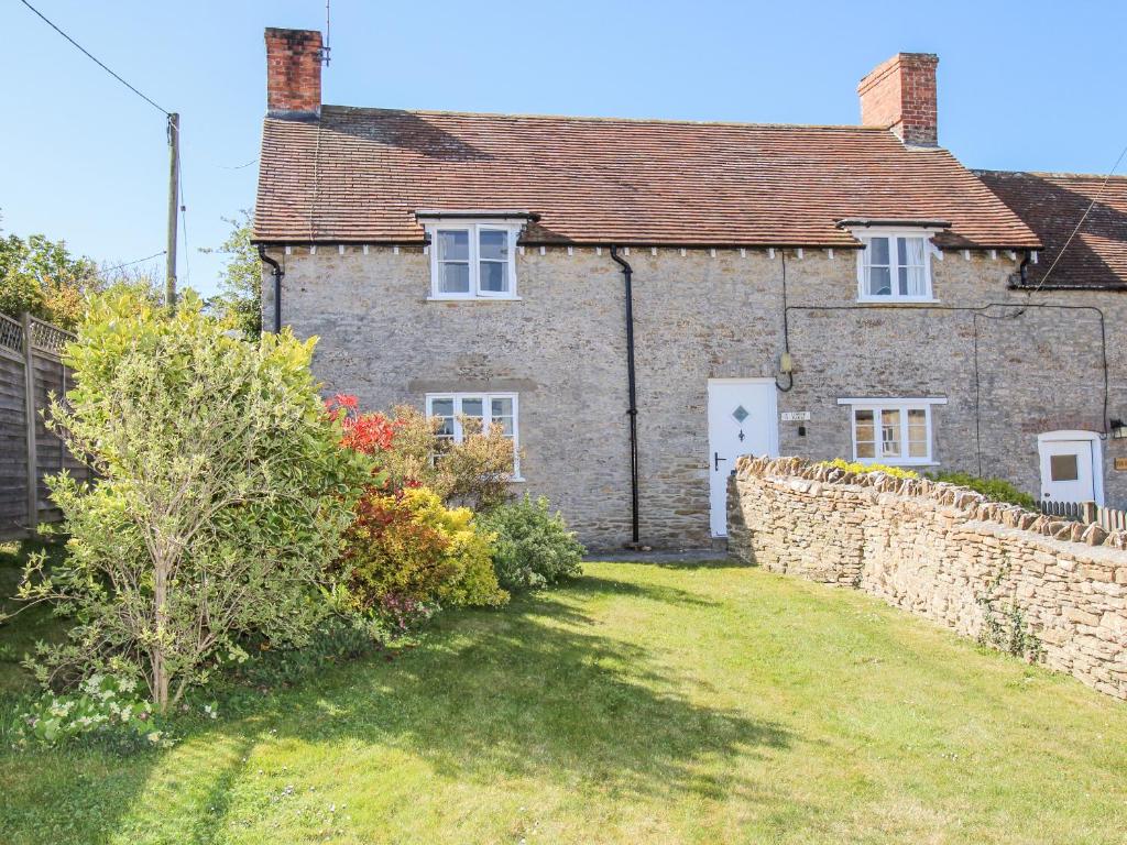 a brick house with a stone wall and a yard at Lower Farm Cottage in Weymouth