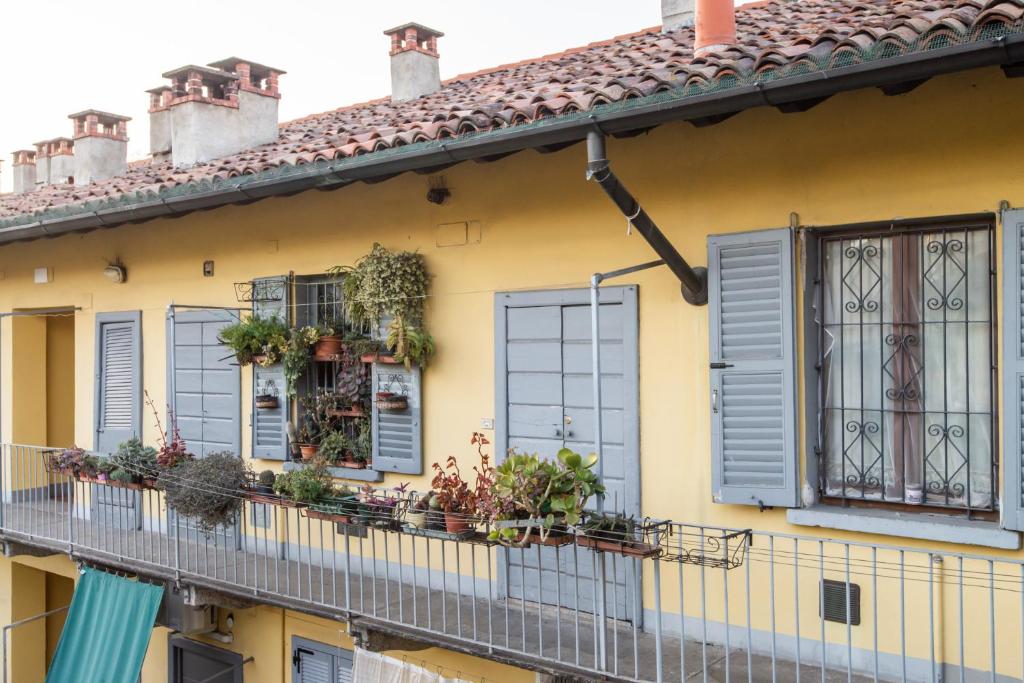 a yellow house with blue shuttered windows and potted plants at Charming Ringhiera Studio in Milan