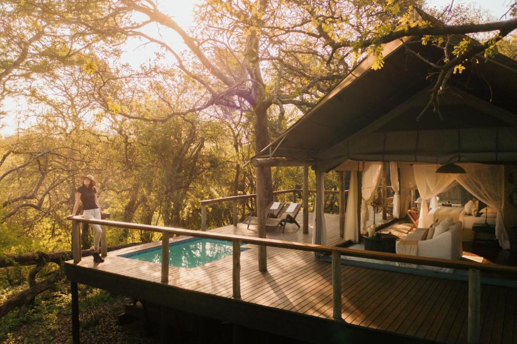 a woman standing on a deck next to a house at Rhino Sands Safari Camp in Manyoni Private Game Reserve