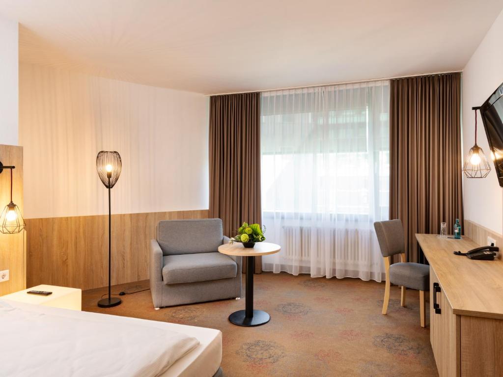 a hotel room with a bed and a chair and a window at Plaza Hotel & Living Frankfurt in Frankfurt/Main