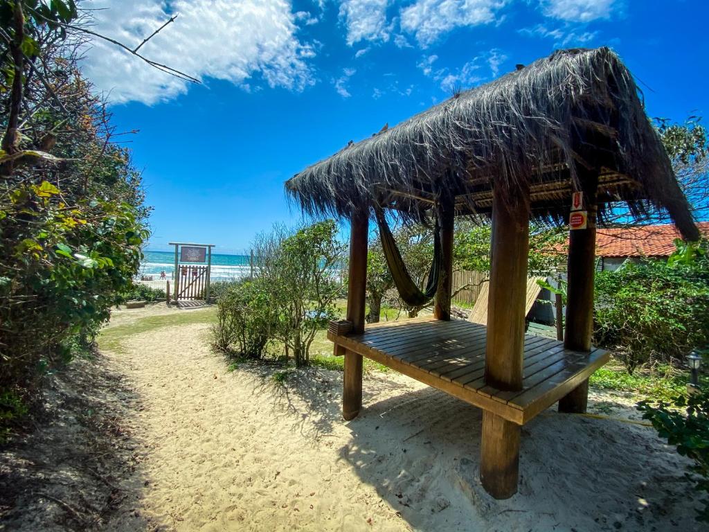 un banco con techo de paja en una playa en The Search House, en Florianópolis