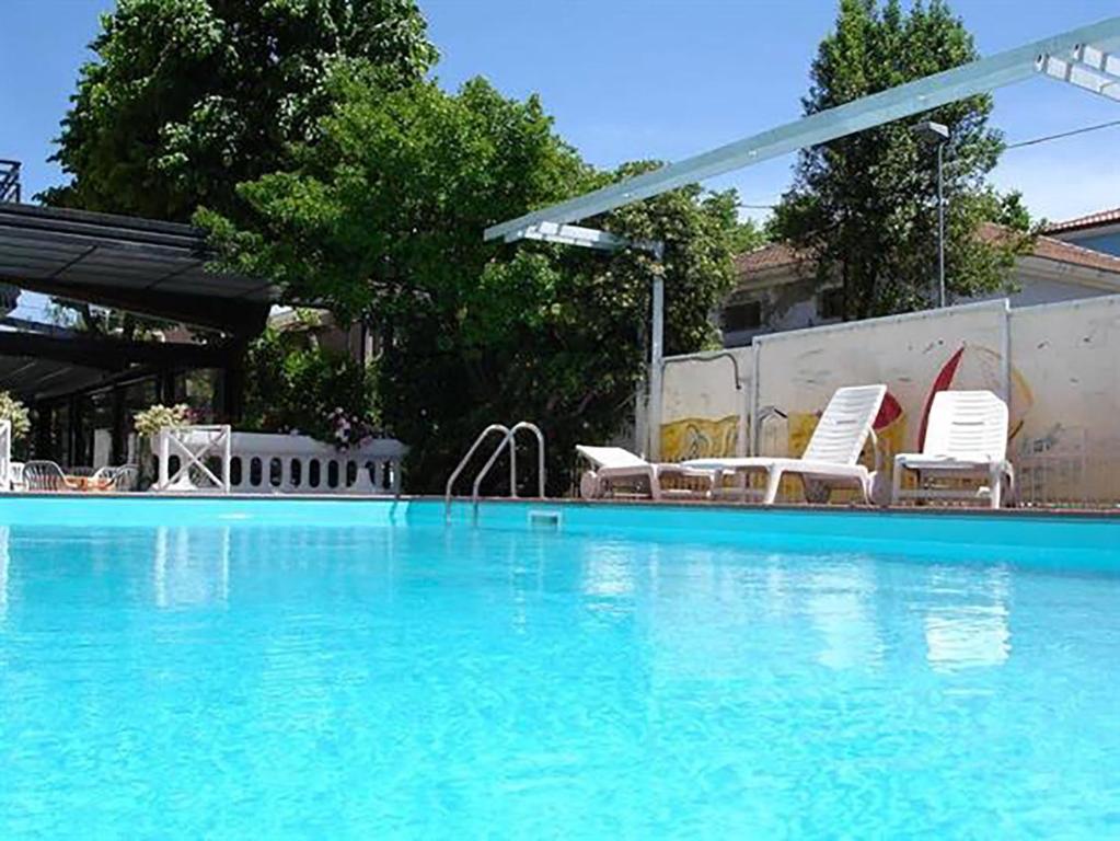 - une piscine avec des chaises blanches dans l'établissement Hotel Apis, à Rimini