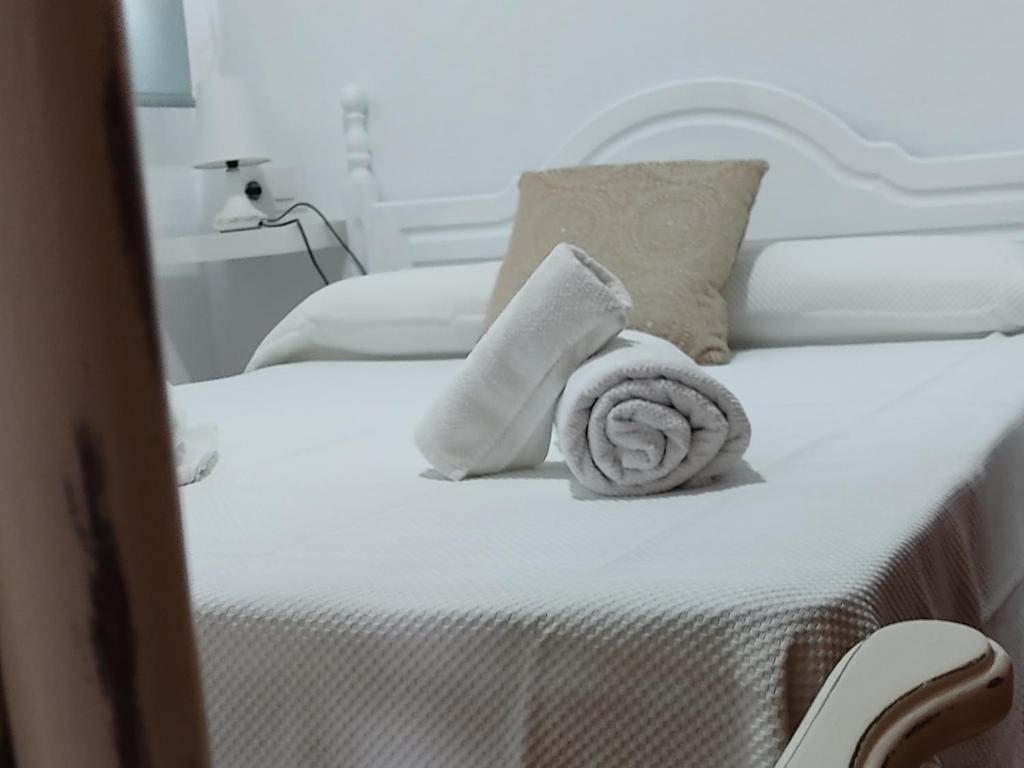 Una cama blanca con una toalla enrollada. en Apartamentos Bolonia - M a n u e l a en Bolonia