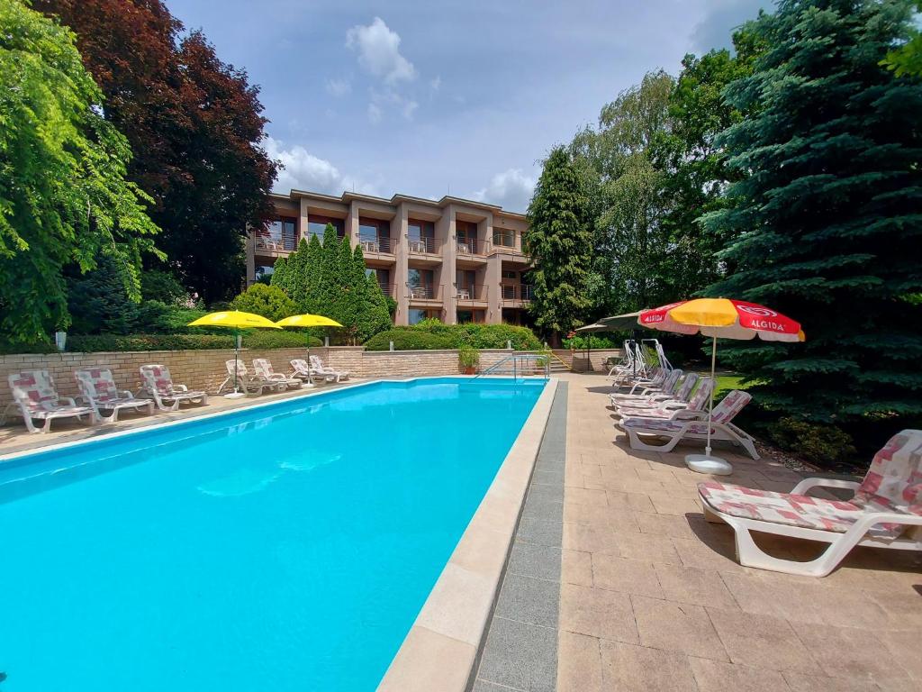 a swimming pool with chairs and umbrellas next to a building at Hotel Villa Pax in Balatonalmádi