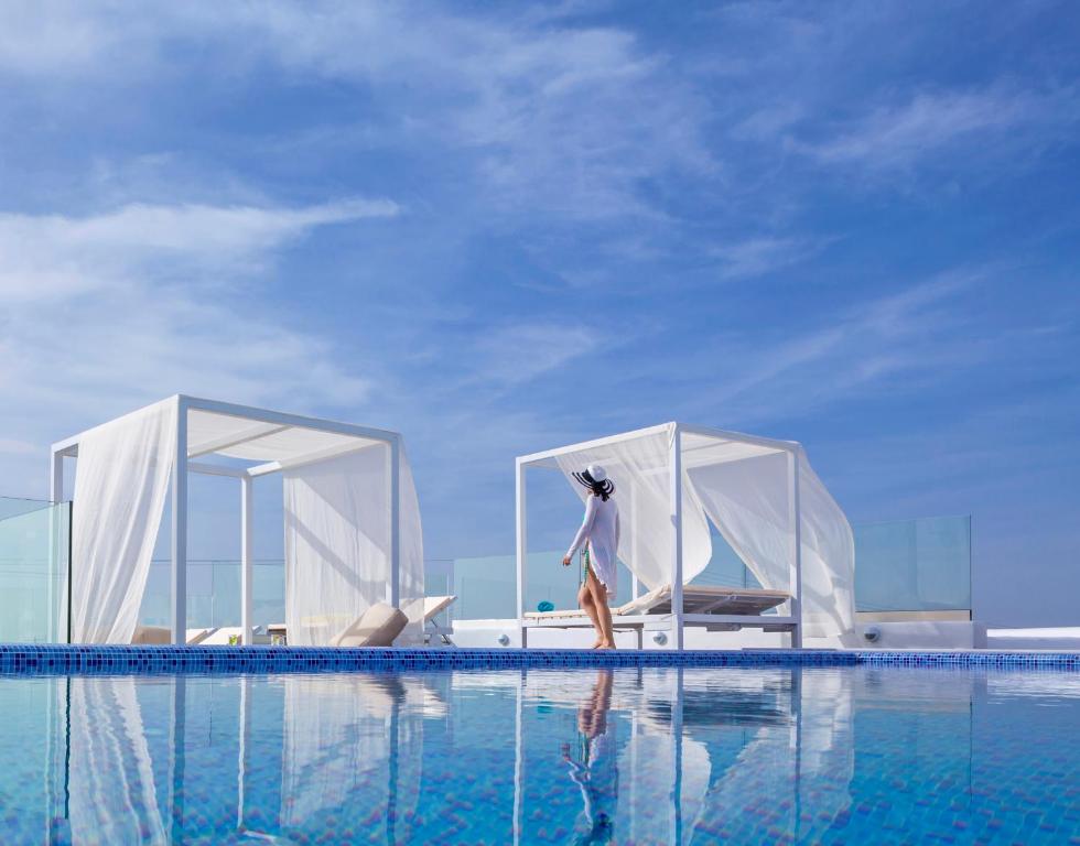 a woman standing on the edge of a swimming pool at Colours of Mykonos Luxury Residences & Suites in Psarou