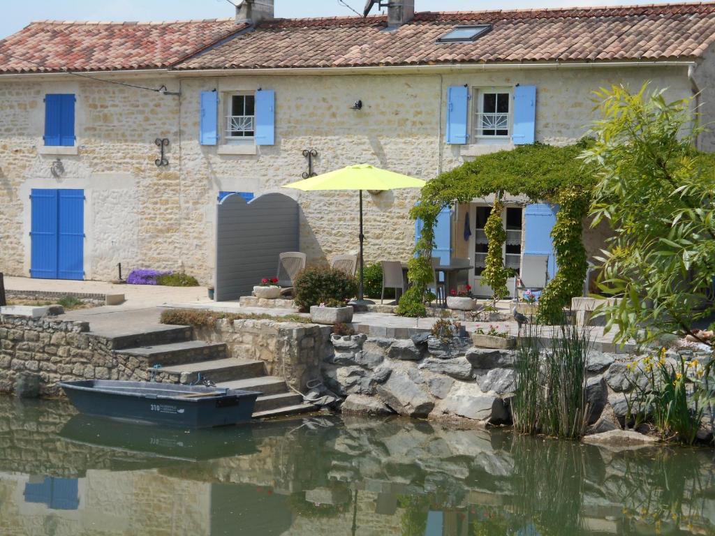 uma casa de pedra com um barco na água em MARAIS POITEVIN gite "volets bleu clair" pêche ,barque, vélos, wifi, linge, cheminée, cuisine, terrain de boules em La Taillée