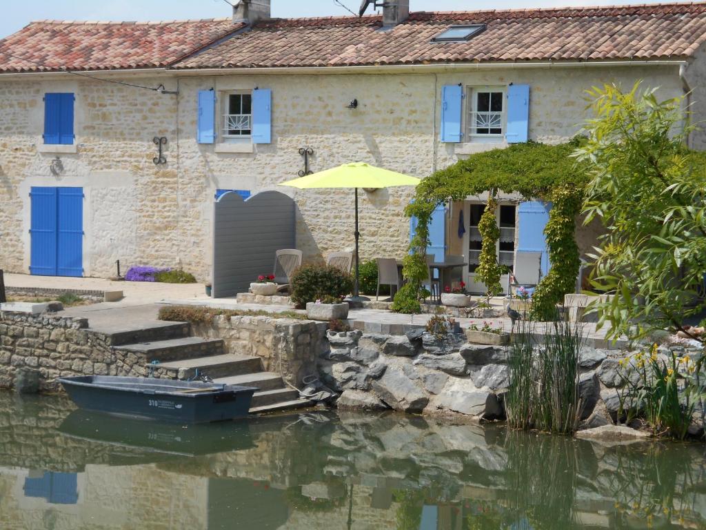 La Taillée的住宿－MARAIS POITEVIN gite "volets bleu clair" pêche ,barque, vélos, wifi, linge, cheminée, cuisine, terrain de boules，水中一艘船的石头房子