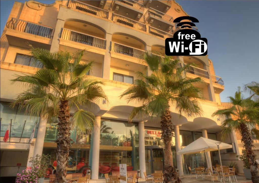 un grand bâtiment avec des palmiers devant lui dans l'établissement Bella Vista Hotel, à San Pawl il-Baħar