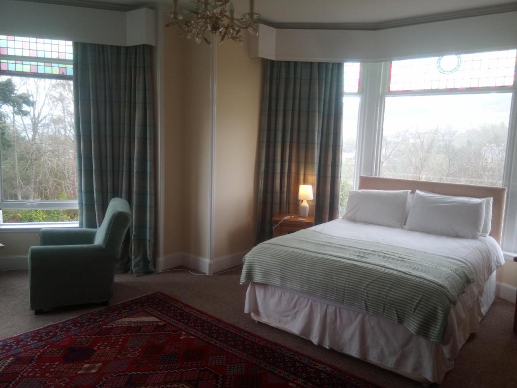 a bedroom with a bed and a chair and windows at Strathview in Strathpeffer