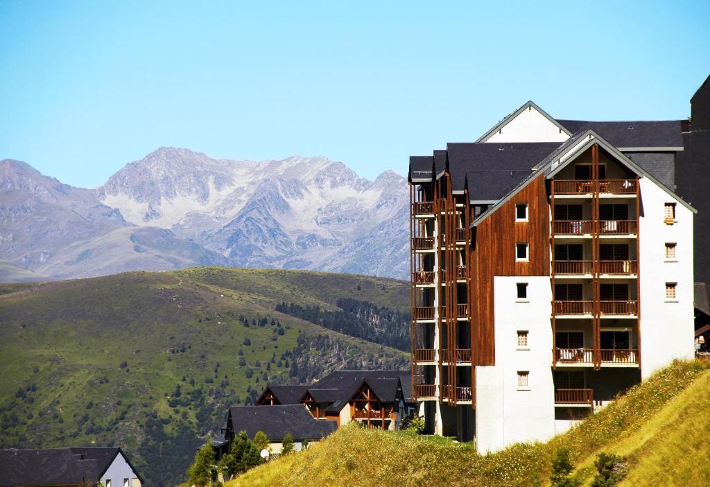 un bâtiment sur une colline avec des montagnes en arrière-plan dans l'établissement Résidence Néméa Royal Peyragudes, à Germ