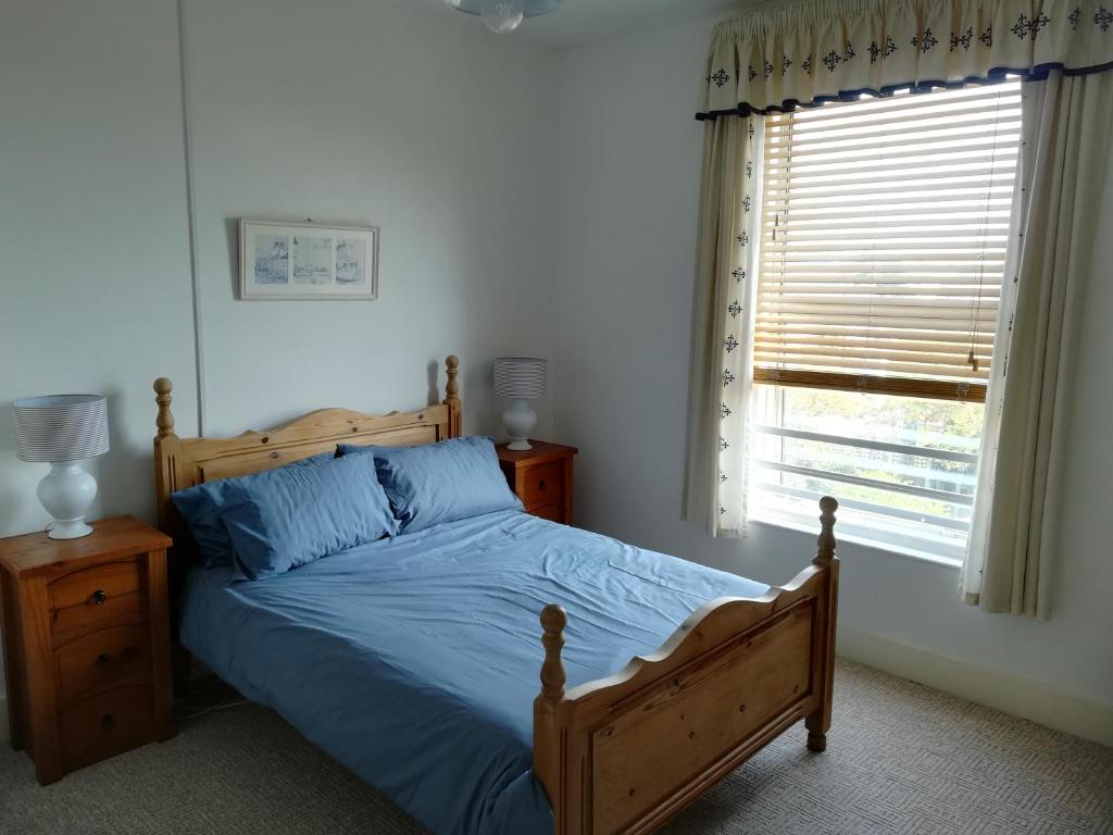Schlafzimmer mit einem Bett mit blauer Bettwäsche und einem Fenster in der Unterkunft Sunrise in Walton-on-the-Naze