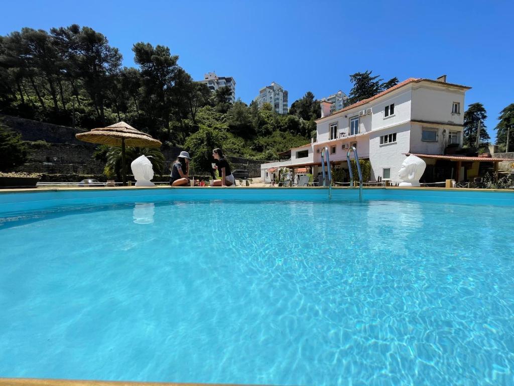 ein großer blauer Pool mit zwei Personen unter einem Sonnenschirm in der Unterkunft Quinta da Villa in Cascais