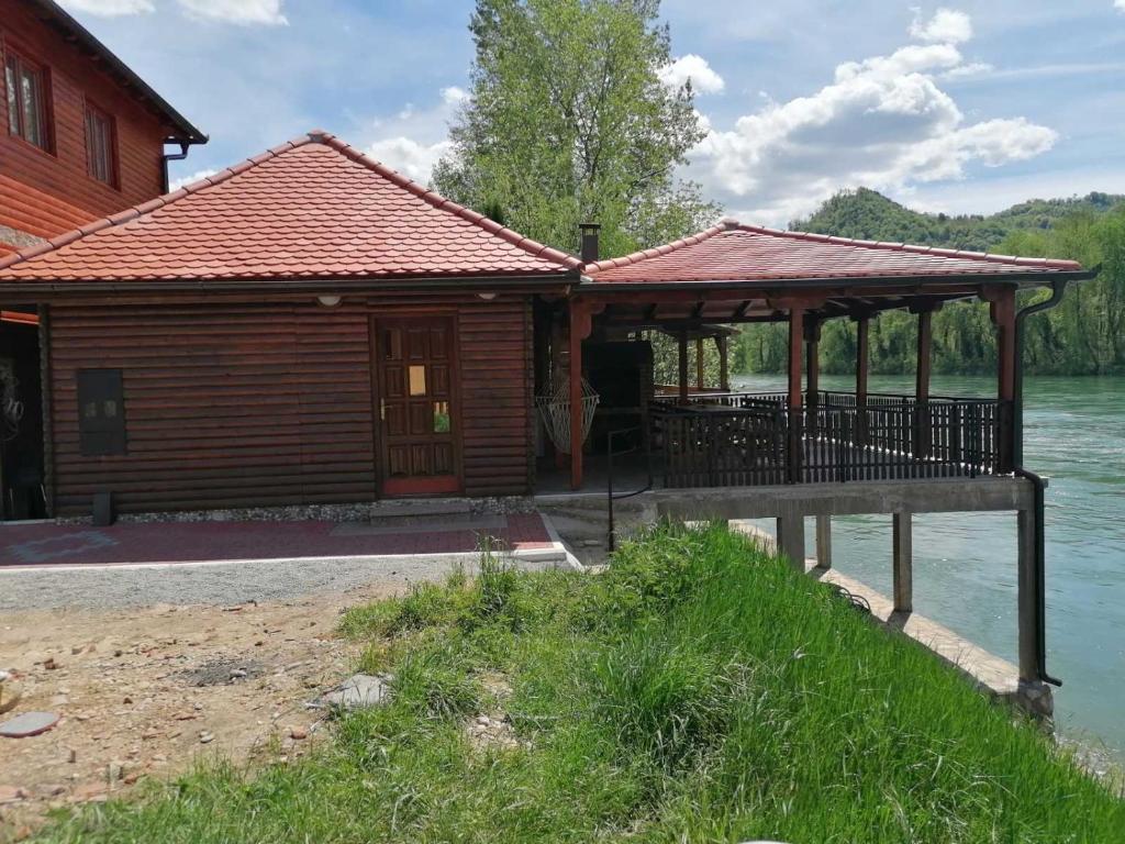 a wooden cabin with a porch next to a river at VIKENDICA ODMOR NA DRINI in Ljubovija