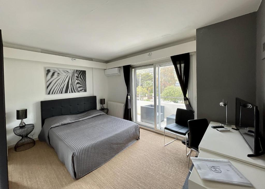 a bedroom with a bed and a desk and a television at Hotel L'Orangeraie in Le Lavandou