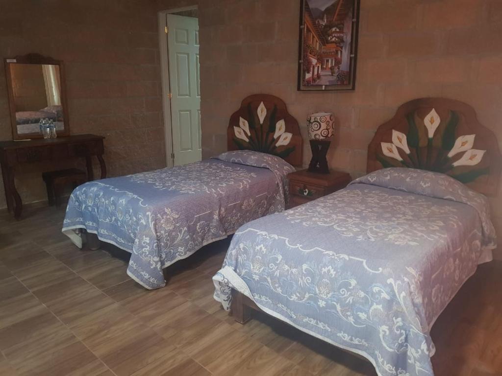 a bedroom with two beds and a table and a mirror at Hotel La Cabaña in San Miguel de Allende