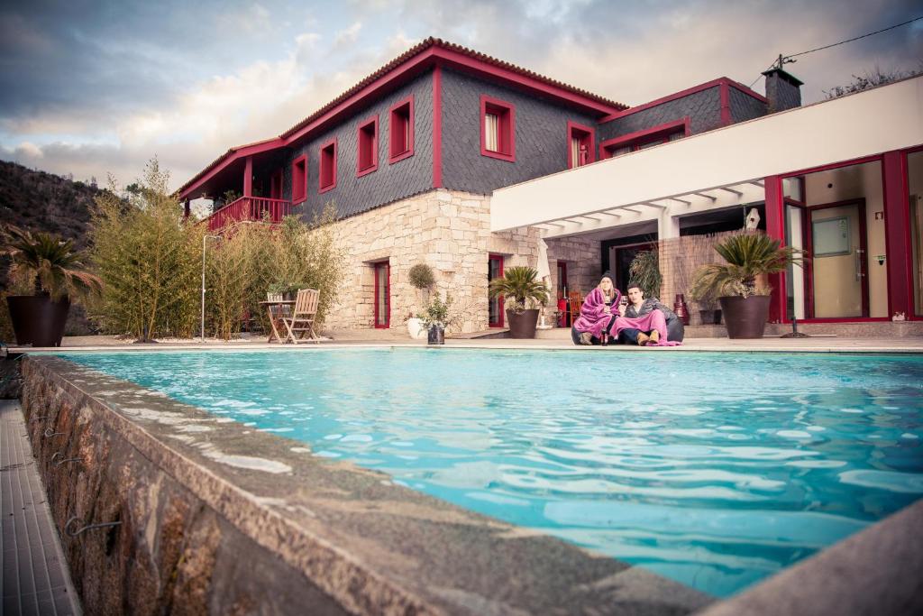 two people sitting by a swimming pool in front of a house at Quinta dos Padres Santos, Agroturismo & Spa in Lamego