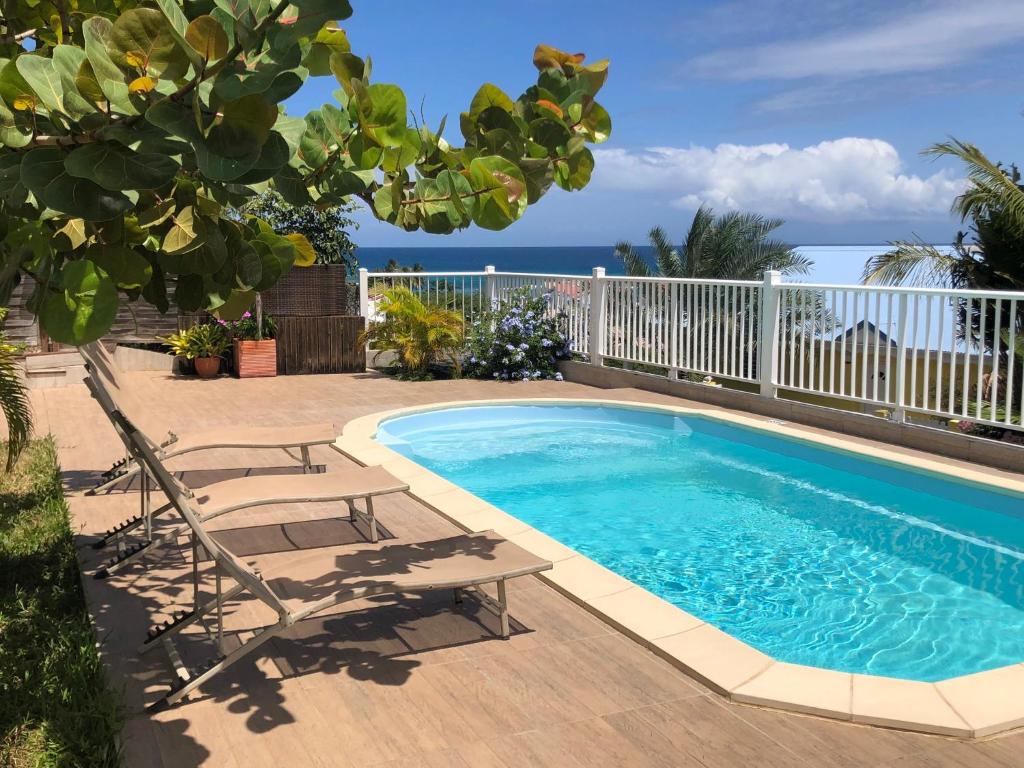 a swimming pool with chairs and the ocean in the background at Mango Sea -Villa "Maracudja" et appartement "Jojoba" avec piscine & vue sur les îles in Saint-François