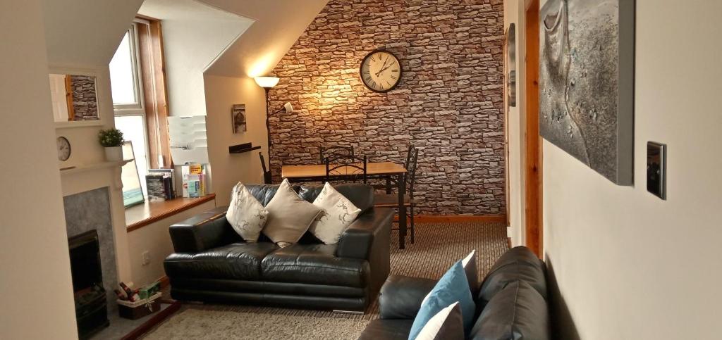 a living room with a couch and a clock on a brick wall at Flat 14c Bayhead in Stornoway