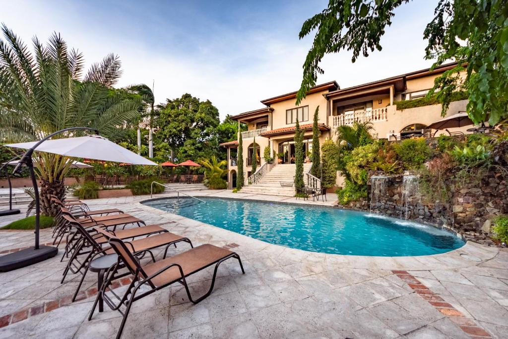 a pool with chairs and an umbrella in front of a house at Hotel Villa Therese in Port-au-Prince