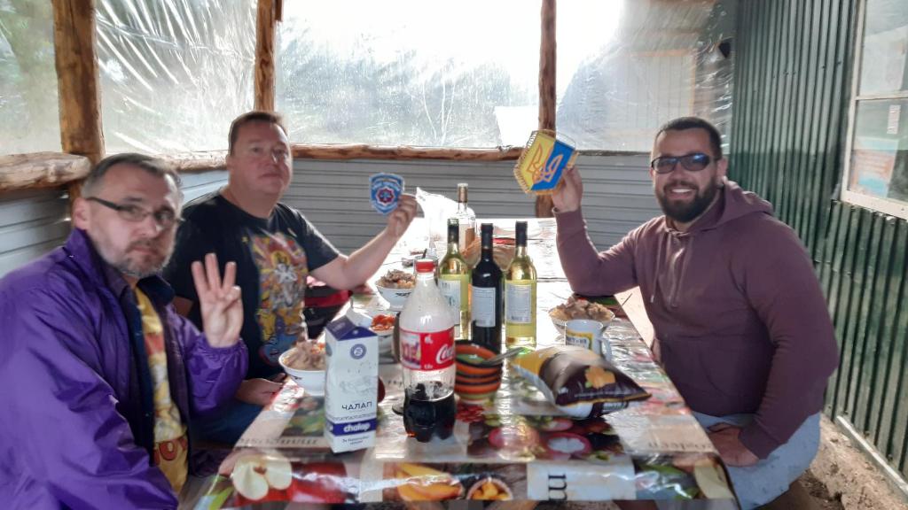 trois hommes assis autour d'une table avec des bouteilles de vin dans l'établissement Алтын-Арашан, путь на оз,Ала-куль, à Teploklyuchinskoye