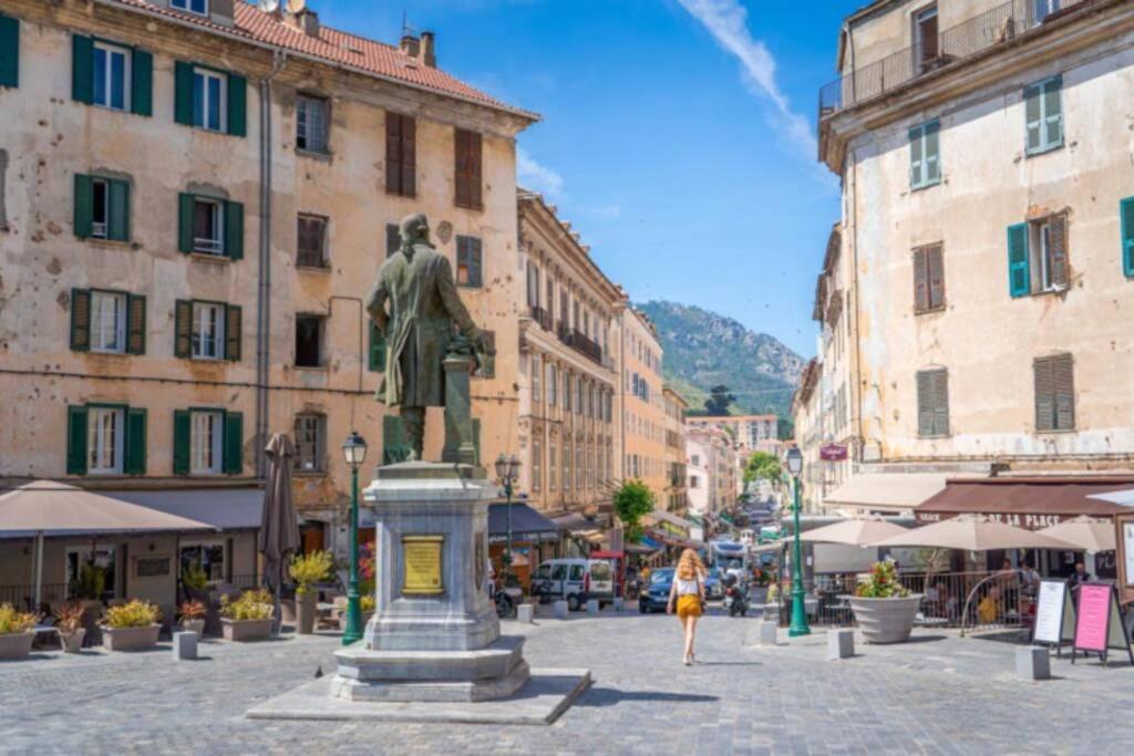 Una mujer caminando por una calle con una estatua en Charmant T3 50m2 plein centre corte 13 cours paoli wifi écran plat lave linge 6 couchages, en Corte