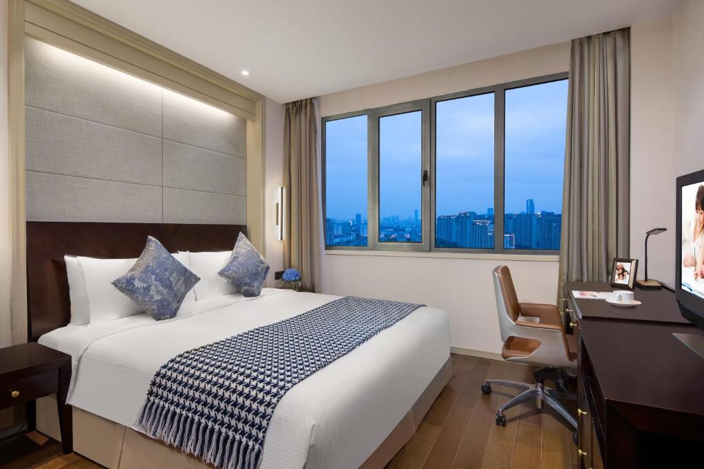 a hotel room with a bed and a desk and windows at Somerset Emerald City Suzhou in Suzhou