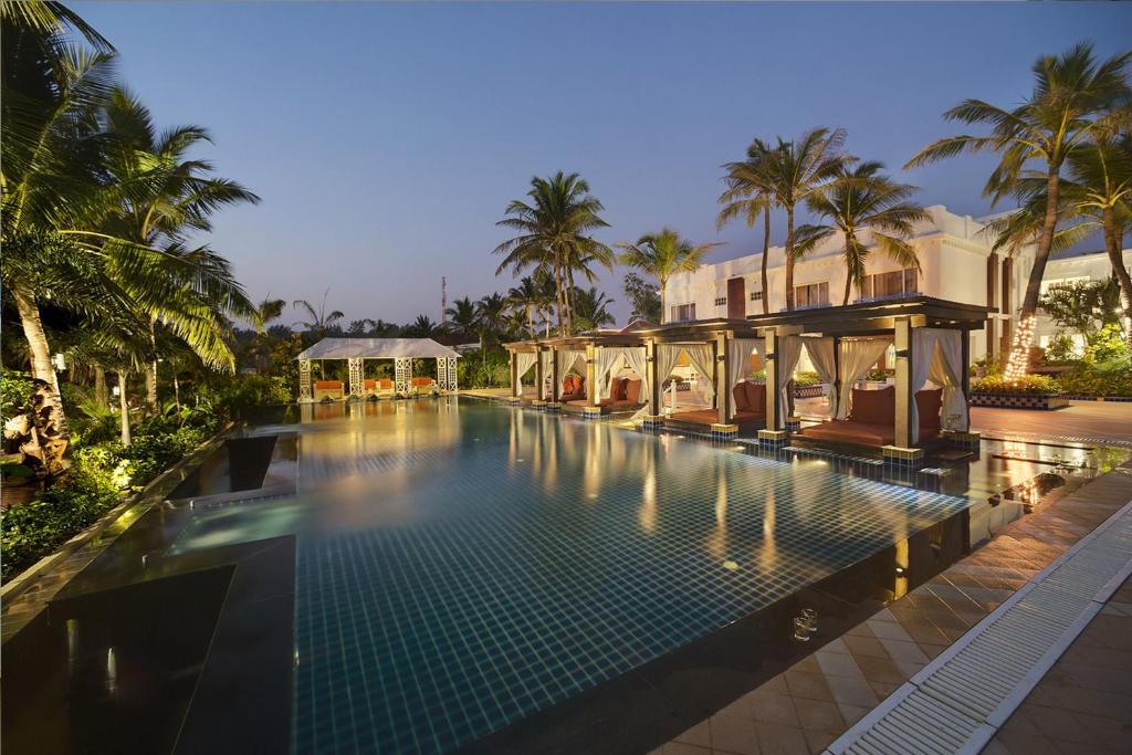 a swimming pool in front of a house with palm trees at Mayfair Palm Beach Resort in Gopālpur