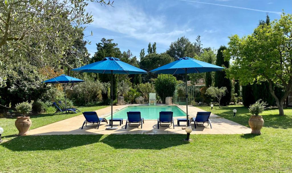 a swimming pool with blue umbrellas and chairs next to a pool at Domaine Au Coeur des Alpilles in Maussane-les-Alpilles