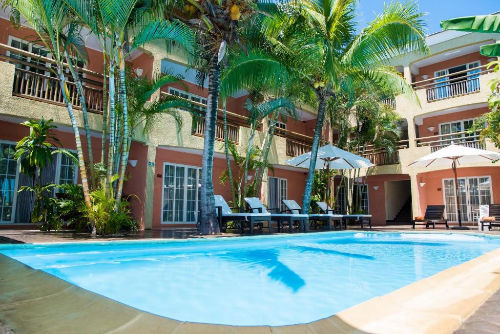 a swimming pool in front of a hotel with palm trees at La Margarita in Pointe aux Piments