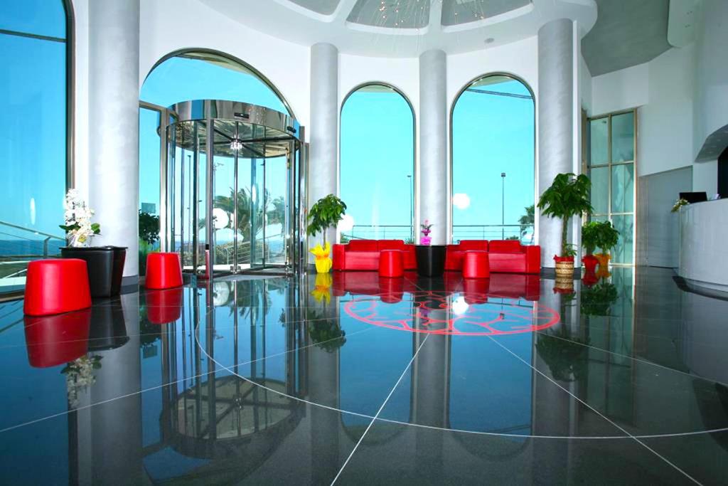 una hall con sedie rosse e una grande stanza con finestre di Jonico Hotel a Torre San Giovanni Ugento