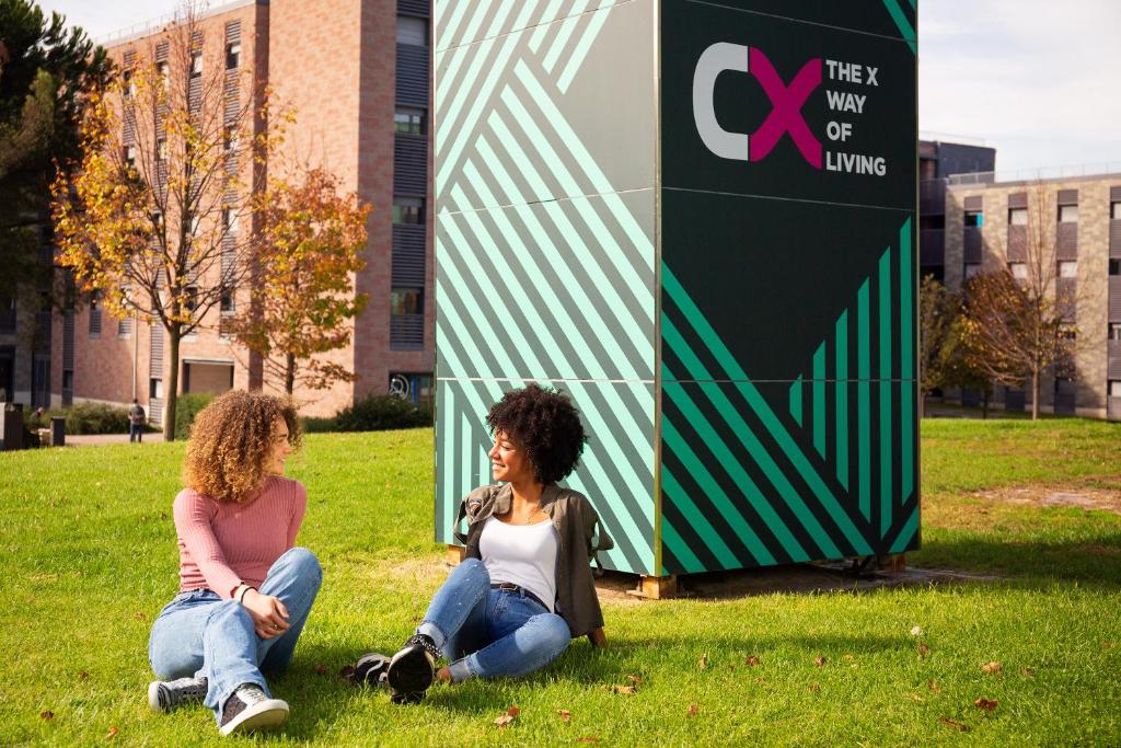 トル・ヴェルガータにあるCX Rome Student Placeの看板の前の芝生に座った二人の女性