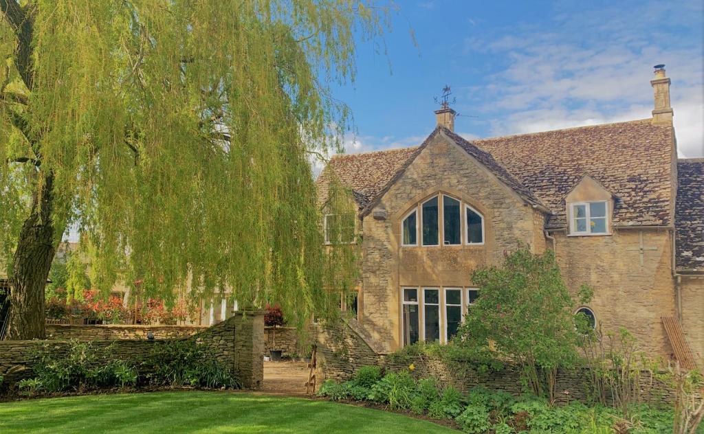 a large stone house with a weeping will tree at Rose Barn Cotswolds with Hot Tub in Langford