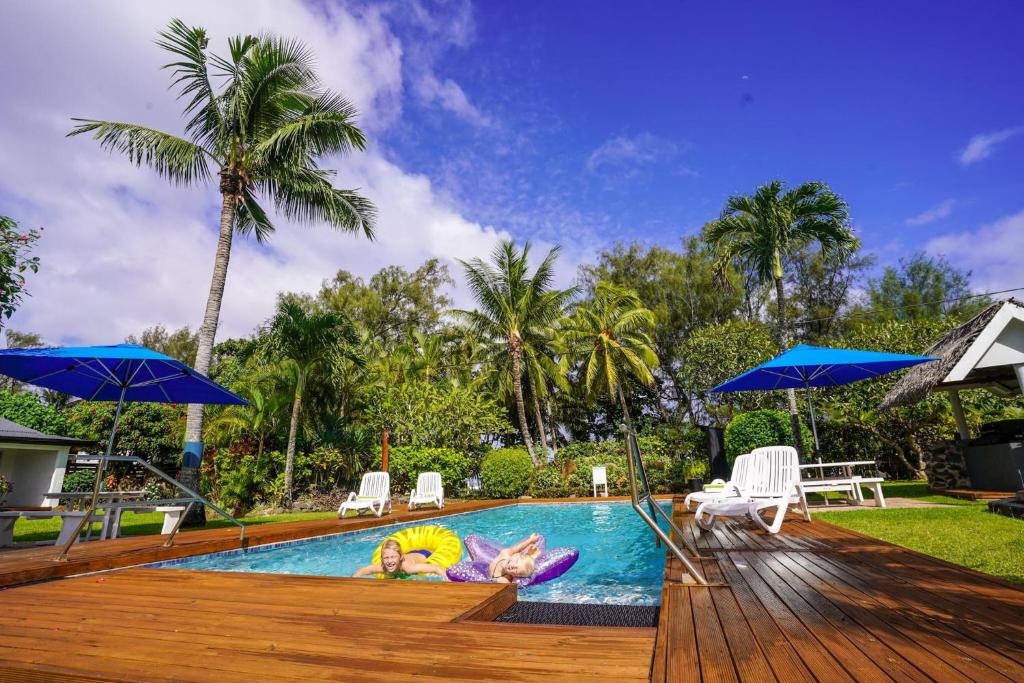 a group of people laying in a swimming pool with umbrellas at The Black Pearl Beachside Apartments in Rarotonga