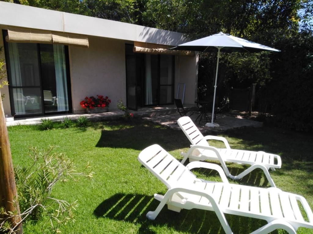 twee witte tuinstoelen en een parasol in een tuin bij Mini casa in Chacras de Coria