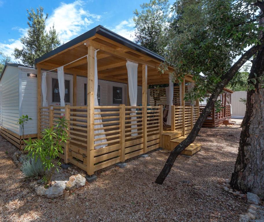 een houten hut met een veranda en een boom bij Mobile Homes Crystal Camp Soline in Biograd na Moru