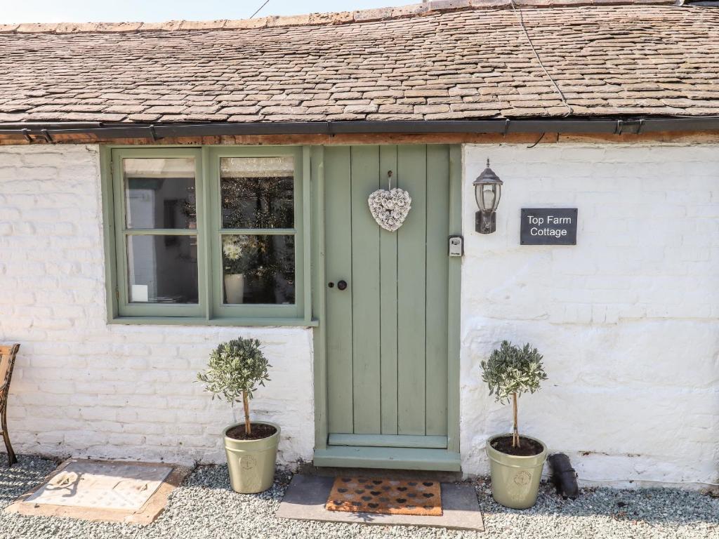 a cottage with a green door and two potted plants at Top Farm Cottage in Oswestry