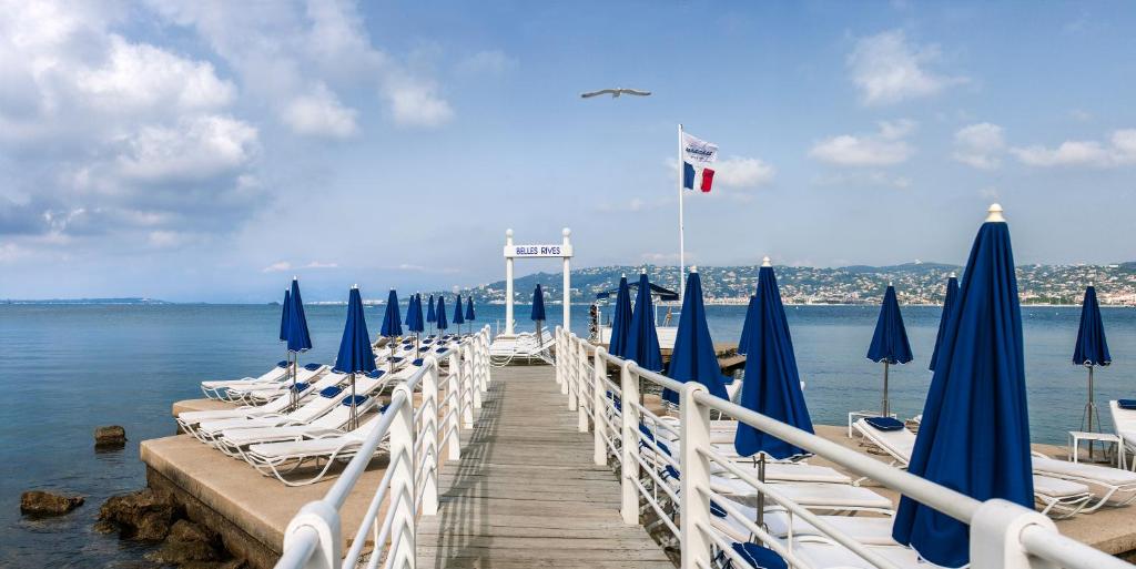 a dock with chairs and blue umbrellas on the water at Hôtel Belles Rives in Juan-les-Pins