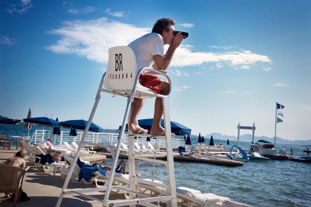 a man sitting in a chair on the beach at Hôtel Belles Rives in Juan-les-Pins