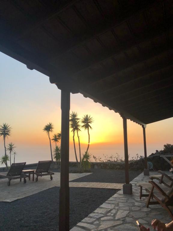 a sunset over the ocean with benches and palm trees at Casa rural Los Llanos Negros in Fuencaliente de la Palma