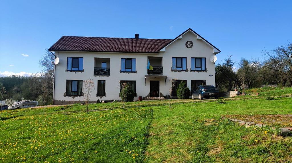 a white house on a hill with a green yard at Hotel Dudarik in Kosiv