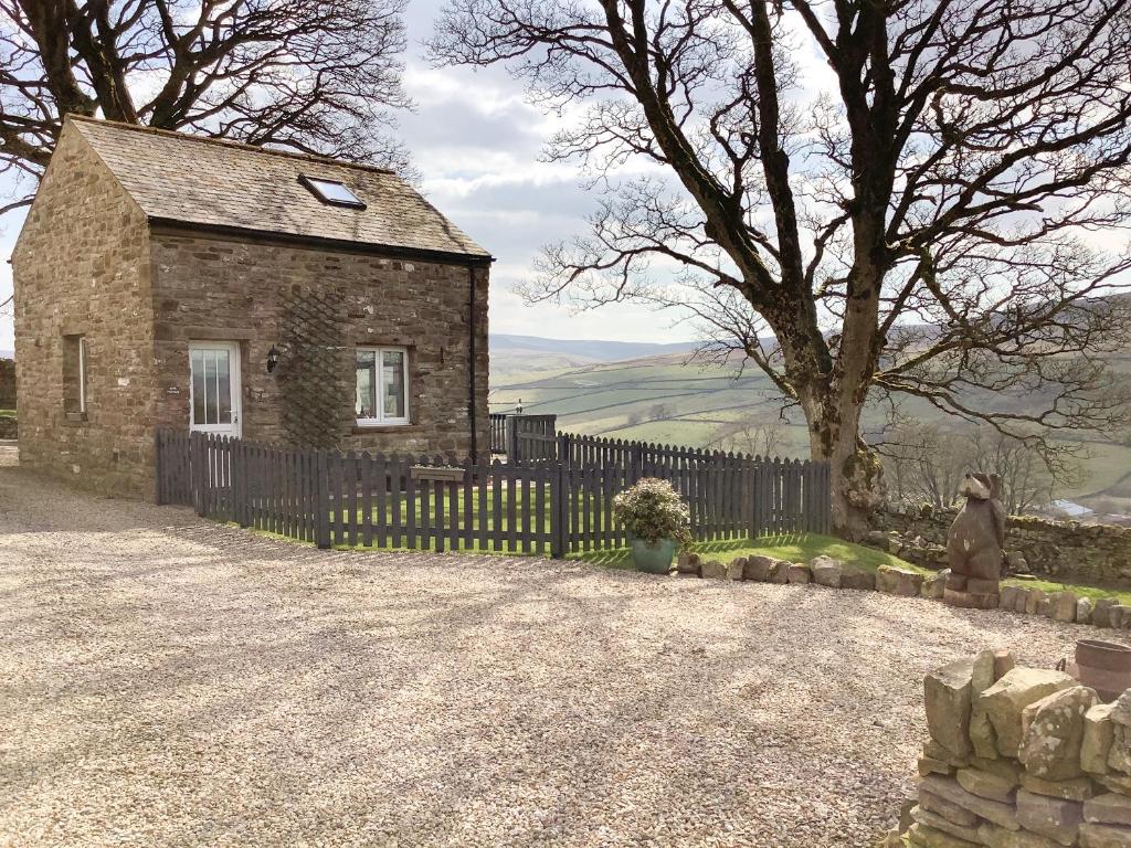 a stone house with a fence and a tree at Byre Cottage in Alston