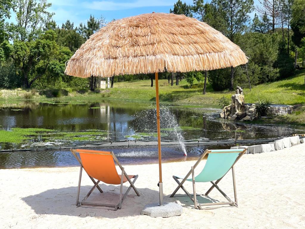 two chairs under a straw umbrella on a beach at DoAguaBoa in Coruche