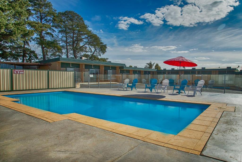 einen Pool mit einem roten Sonnenschirm und Stühlen sowie eine Terrasse in der Unterkunft Hi Way Eight Motor Inn in Stawell